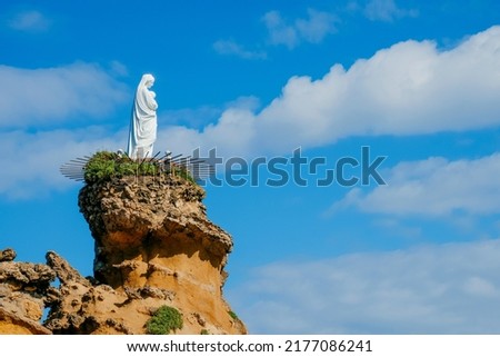 a detail of the Rocher de la Vierge in Biarritz, France, a rock formation in the ocean topped with the image of the Virgin Mary, against the sky