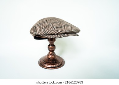 Detail Of Scally Cap Or Flat Cap In Dark Brown Pattern Herringbone Tweed Fabric Set On A Bronze Head Mannequin On A White Background