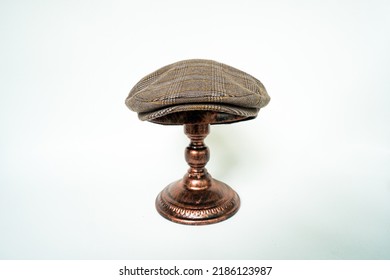 Detail Of Scally Cap Or Flat Cap In Dark Brown Pattern Herringbone Tweed Fabric Set On A Bronze Head Mannequin On A White Background