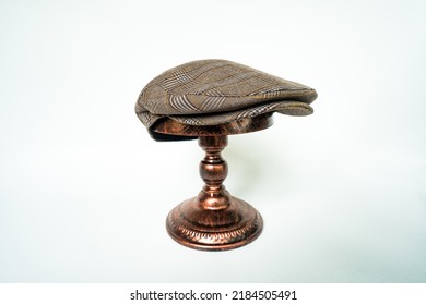 Detail Of Scally Or Flat Cap In Dark Brown Pattern  Herringbone Tweed Fabric Set On A Bronze Head Mannequin On A White Background