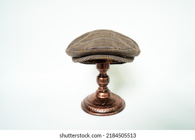 Detail Of Scally Or Flat Cap In Dark Brown Pattern  Herringbone Tweed Fabric Set On A Bronze Head Mannequin On A White Background