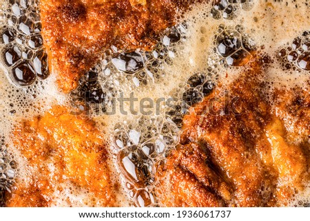 Detail of schnitzels in breadcrumbs sizzling in frying oil.