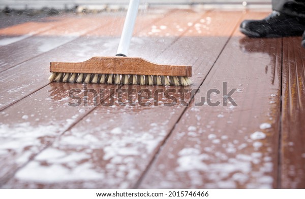 Detail of a scrubbing\
brush during spring cleaning on a wooden terrace with soap and\
splashes of water