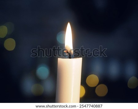 Detail shot of a candle with a blurred (bokeh) background. Warm flame contrasted with cold, dark blue background.