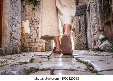 Detail shot of female legs wearing comfortable travel sandals walking on old medieval cobblestones street dring sightseeing city tour. Travel, tourism, and adventure concept.