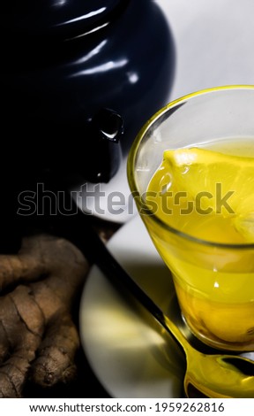Detail shot of a glass cup with ginger and lemon tea, on a wooden table and a blue teapot. Concept of homeopathy and traditional medicine