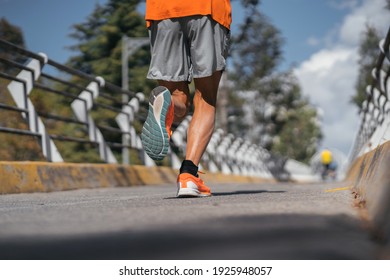 Detail Shot Of A Grown Man Running On An Urban Track. He Wears Orange Tennis Shoes And An Orange Shirt