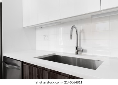 A Detail Shot Of A Kitchen Sink With White And Wood Modern Cabinets, Chrome Faucet, And Subway Tile Backsplash.