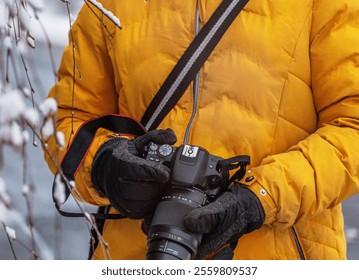 Detail shot of a person hands wearing  gloves holding a DSLR camera adjusting  lens settings, dressed warmly in yellow during a winter outdoor photoshoot. - Powered by Shutterstock