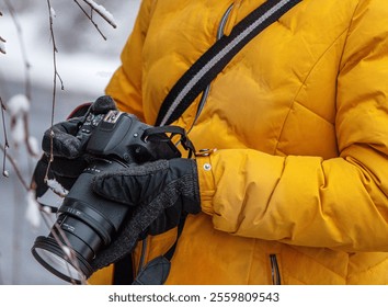 Detail shot of a person hands wearing  gloves holding a DSLR camera adjusting  lens settings, dressed warmly in yellow during a winter outdoor photoshoot. - Powered by Shutterstock