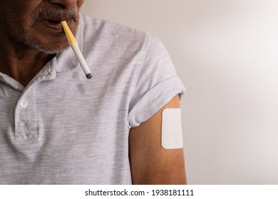 Detail Shot Of The Shoulder Of An Elderly Caucasian Man, With A Menthol Cigarette To Quit Smoking In His Mouth And A Nicotine Patch On His Arm, Following A Smoking Cessation Treatment.