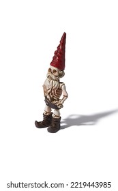 Detail Side Shot Of A Designer Figurine Of A Skeleton Of A Dwarf Man In A Red Hat And A Brown Loincloth. The Original Handmade Statuette Is Isolated On The White Background.                           