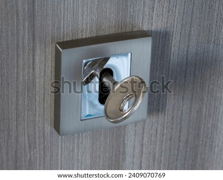 Detail of a silver key stuck in a modern silver lock. Gray wooden door.