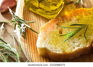 Detail of a slice of bread seasoned with rosemary-essenced oil on a wooden plate with rosemary sprigs and oil bottle. Top view. - Powered by Shutterstock