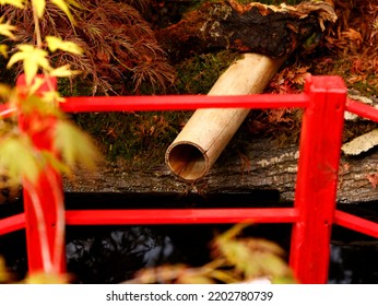 Detail Of A Small Red Bridge And A Bamboo Pipe Seen In A Japanese Style Planted Garden In The UK.