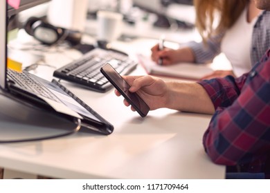 Detail of software developers working in an office, taking notes on a morning briefing, woman writing in a planner while man typing notes on a smart phone
