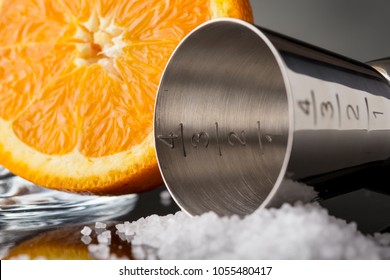 Detail of some salt, orange fruit and cocktail jigger next to it. Selective focus on the jigger numbers scale