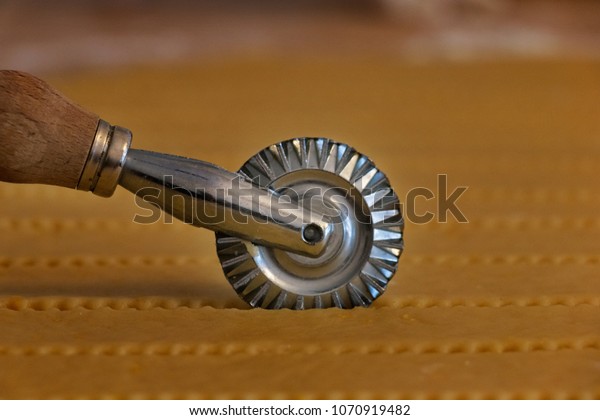 Detail of a  steel pastry cutter wheel while
cuts a layer of puff pastry. The cut is serrated , horizontal
composition ,out of focus
background
