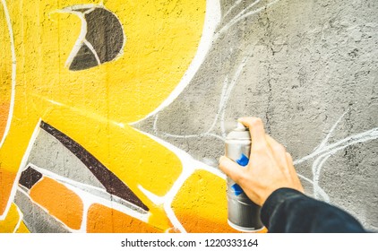 Detail of street artist painting colorful graffiti on public wall - Modern art concept with urban guy drawing live murales with multi color aerosol spray - Vintage filter with focus on yellow paint - Powered by Shutterstock