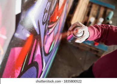 Detail of street artist painting colorful graffiti on public wall. Modern art concept with urban guy drawing live murales with multi color aerosol spray. Focus on the boy hand with spray paint can