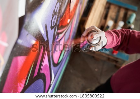Detail of street artist painting colorful graffiti on public wall. Modern art concept with urban guy drawing live murales with multi color aerosol spray. Focus on the boy hand with spray paint can