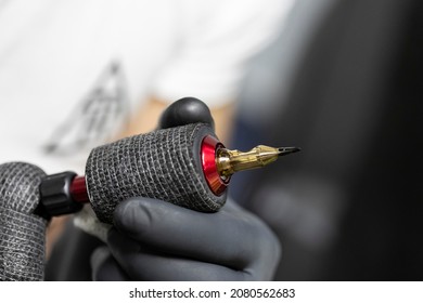 Detail of the tattooist's hand with black glove holding the tattoo machine while regulating the needles during a job. Image in horizontal and colour. Tattoo concept.