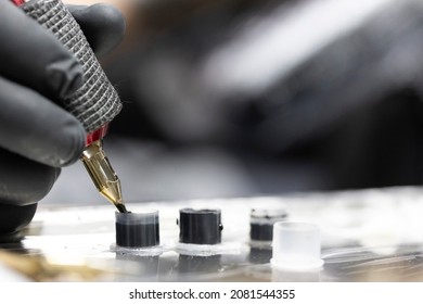 Detail of the tattooist's hand with black glove holding the tattoo machine while he loads ink into the needle while performing a tattoo. Image in horizontal and colour.