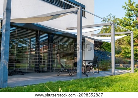 Detail of terrace of modern, white, cube, elegant, minimalist style passive house with large panoramic windows, grey shutters in maintained garden.