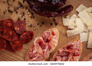 Detail top view of a delicious appetizer shot on a rustic wooden table, with a varied composition that contains Spanish tapas of Iberico ham, chorizo, slabs of cheese, peppercorns and peppers - Powered by Shutterstock