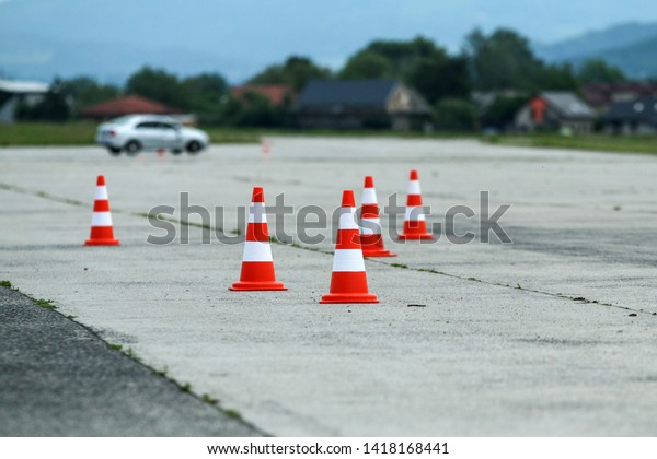 The detail of the traffic cones on the concrete area.\
They are used for testing of the cars. The blurred car is behind\
the cones. 