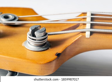 Detail of a tuning post on the wooden headstock of an electric bass guitar. Musical instruments and mechanics for string tuning.