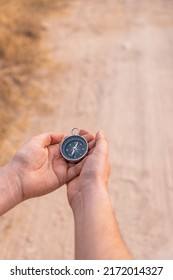 Detail Of Two Hands Holding A Compass, On A Dirt Road. Vertical Photography, With Copy Space.