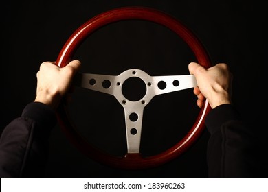 Detail Of Two Hands Holding A Wooden Vintage Steering Wheel On Black.