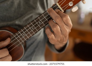 Detail of unrecognizable man's hand playing a chord on the ukulele