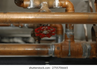 Detail view of a complex copper pipe system with a vibrant red valve. Industrial and worn