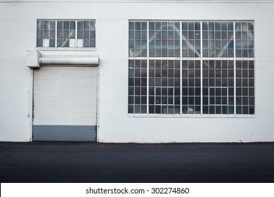 Detail Of Warehouse Building With White Walls, Rolling Door And Large Window Taken Straight From The Front