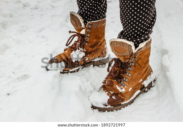 Detail of warm winter boots in snow.Female feet in\
brown shoes, winter walking in snow.Low angle view of standing\
female legs with  snowy boots. Winter scenic background copy\
space.Pair of shoes