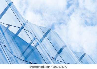 Detail of the wavy glass curtain wall facade of a nice modern building, sky and clouds reflecting on it