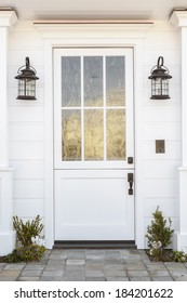 Detail Of A White Front Door To A Classic White Family Home. Door Features Intricate Etched Detail. Also Seen Is Columns, A Stone Porch, And Light Fixtures. 