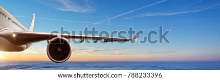 Detail of wing of commercial airplane jetliner flying above clouds in beautiful sunset light. Travel and business concept