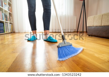 Detail of woman doing housework, holding a broom and sweeping floor