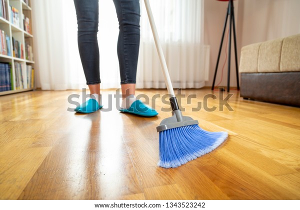 Detail of woman doing housework, holding a broom\
and sweeping floor