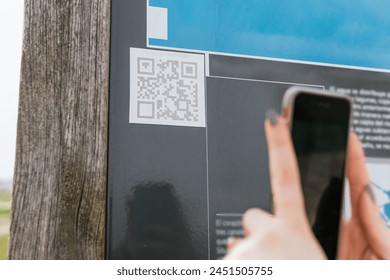 Detail of woman scanning a QR code on an information panel with her mobile phone