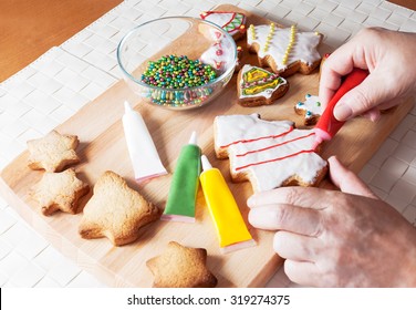 A Detail Of A Woman's Hand Which Is Decorating Christmas Cookie In Shape Of Christmas Tree With Red Ornaments