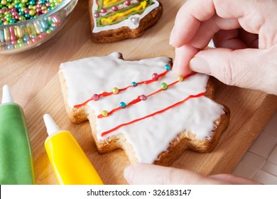 A Detail Of A Woman's Hand Which Is Decorating Christmas Cookie In Shape Of Christmas Tree With Sugar Balls. Selective Focus