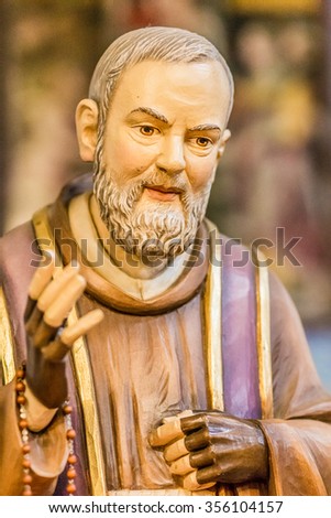 detail of a wood carved statue of Saint Father Pius with his gloved hands to cover the stigmata while holding a rosary