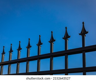 Detail of wrought iron fence. Decorative Steel Gate against blue sky. Street photo, nobody, selective focus.
