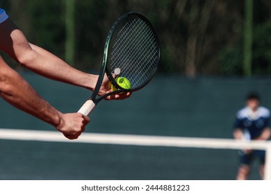 Detail of young boy with racket playing tennis on a clay court during a university tournament. the athlete is wearing a blue sports t-shirt and is preparing to serve for set point - Powered by Shutterstock