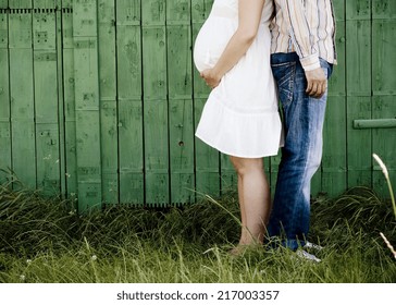 Detail of young pregnant couple in front of green fence in nature