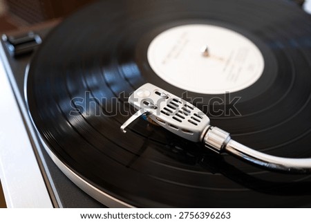 A detailed, angled shot of a silver headshell and stylus tracking the grooves of a black vinyl record in motion